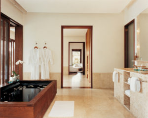 Interior of the bathroom at Como Shambhala’s Taramala villa with two hanging bathrobes and a filled bath with flowers