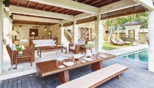 Living and dining area of the Giri Antara 3 bedroom home at Como Shambhala featuring sofas and coffee tables, and long bench-style table and seating, with view of the pool and garden terrace in the background