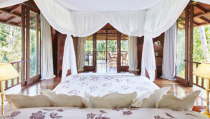 Master bedroom at the Pita Linggar 3 bedroom home featuring canopy bed and french doors leading off to a terrace with panoramic jungle views