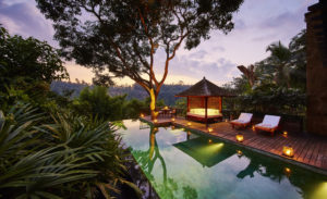 The swimming pool in the middle of the Bali jungle at the Sukma Taru 2 bedroom home at dusk surrounded by lamps highlighting the patio area with swing seating and lounge beds