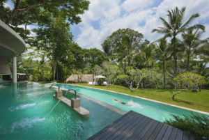 Como Shambhala’s vitality pool with a man taking laps in the pool below and the Bali jungle in the background