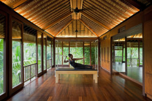 Female practising pilates in Como Shambhala’s pilates studio with wooden features and a view of the Bali jungle out of the windows